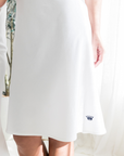 White dress with a small navy crown logo on a light background