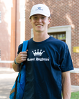 Person wearing a navy blue 'Royal Highness' t-shirt with a white cap, standing outdoors.