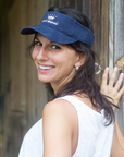 A woman wearing a navy blue visor with the 'Highnies' logo on it, smiling and standing in front of a wooden structure.