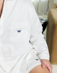 Person wearing a white long sleeve shirt with a small navy logo, sitting indoors.