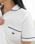 Woman wearing a white polo shirt with navy trim and crown logo, close-up on chest area.