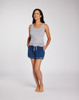 Woman wearing a light gray tank top and navy blue drawstring shorts, photographed against a clean light gray studio background.