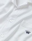 Close-up of a white long-sleeve button-up shirt with a chest pocket featuring a small navy embroidered crown logo.