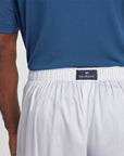 Close-up of a person wearing white lounge pants with a black elastic waistband and a visible Royal Highnies label, paired with a blue shirt against a light gray background.