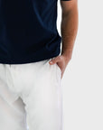 Close-up of a person wearing a dark navy short-sleeve top and white pants, with the hand tucked into the pocket of the pants, against a light gray background.
