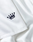Close-up of a white fabric garment with a small navy embroidered crown logo on the sleeve.