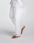 White lounge pants worn by a model, shown from the waist down in a side profile against a light gray studio background. A small navy crown logo is visible near the ankle.