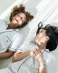 Two women in matching white tops lying on a white floor.