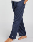 A person wearing navy blue lounge pants, shown from the waist down against a light gray studio background. The pants are loose-fit with a small white crown logo near the left ankle.
