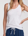 Woman wearing a white tank top and navy drawstring shorts, photographed against a clean light gray studio background.