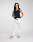 A woman modeling a two-piece loungewear set consisting of a navy tank top and white drawstring pants with thin navy piping details, shot against a light gray studio background.