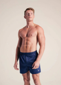 Man wearing navy boxers with white logo against a plain background