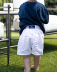 Child wearing a navy blue shirt and white shorts with a visible Royal Highnies label, standing on grass.