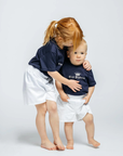 Two children wearing navy blue shirts with white text on a light gray background