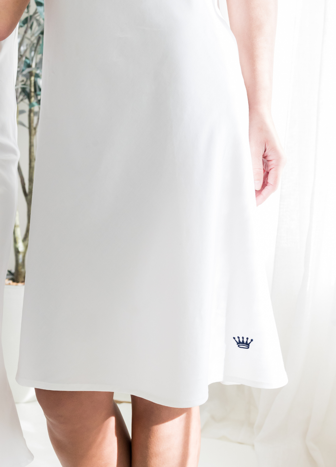 White dress with a small navy crown logo on a light background