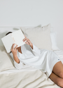 Person lying on a bed reading a book in a white dress.