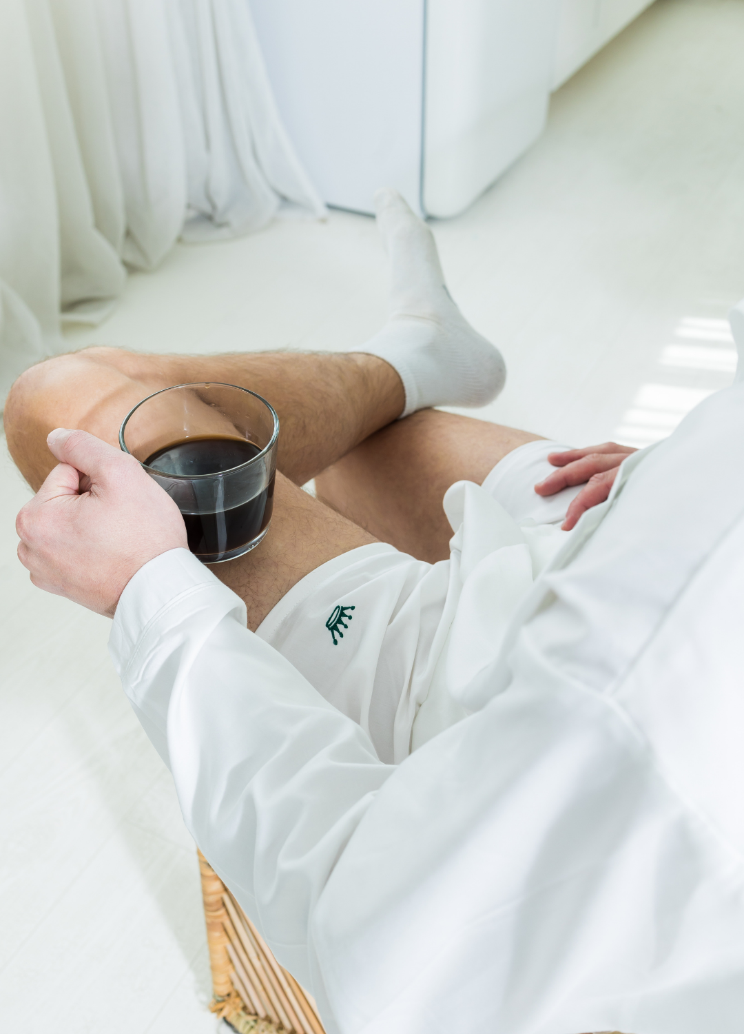 Person wearing white boxer shorts with green embroidery, holding a cup of coffee