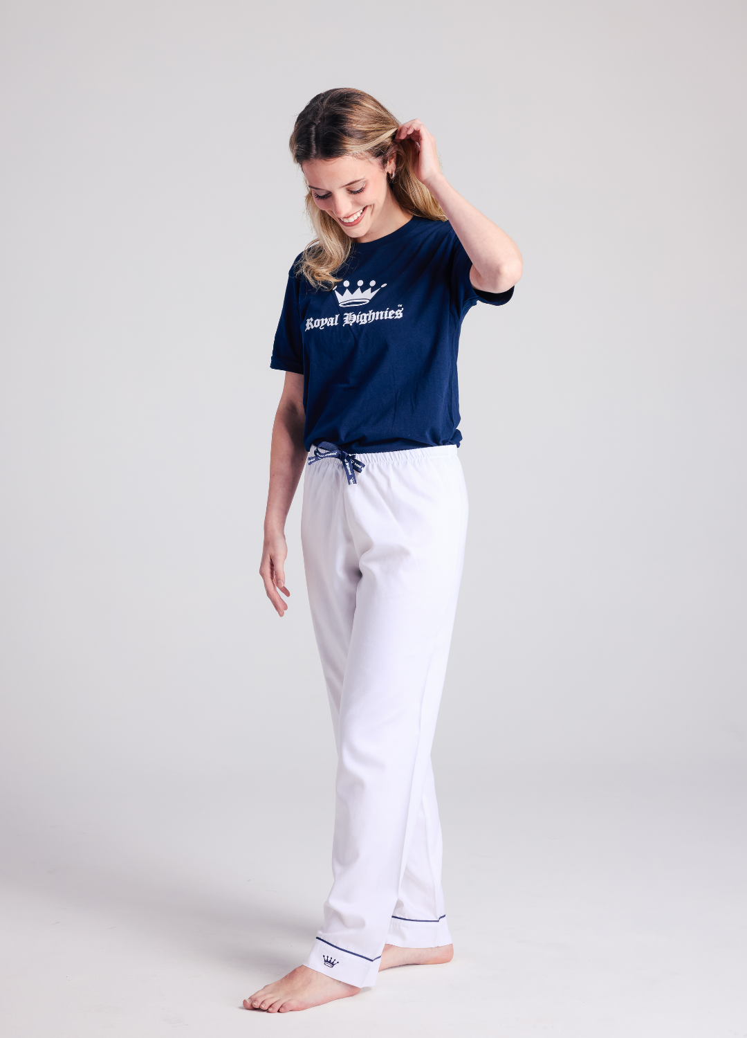 Woman wearing a navy blue t-shirt with a logo and white pants on a light gray background