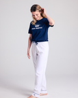 Woman wearing a navy blue t-shirt with a logo and white pants on a light gray background