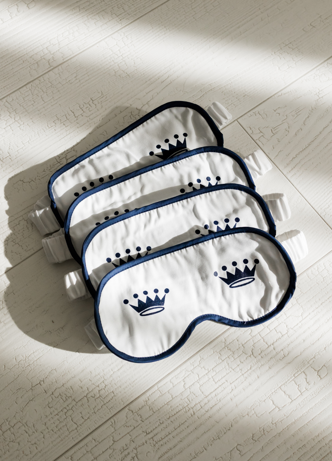 Four sleep masks with a crown logo on a light wooden floor