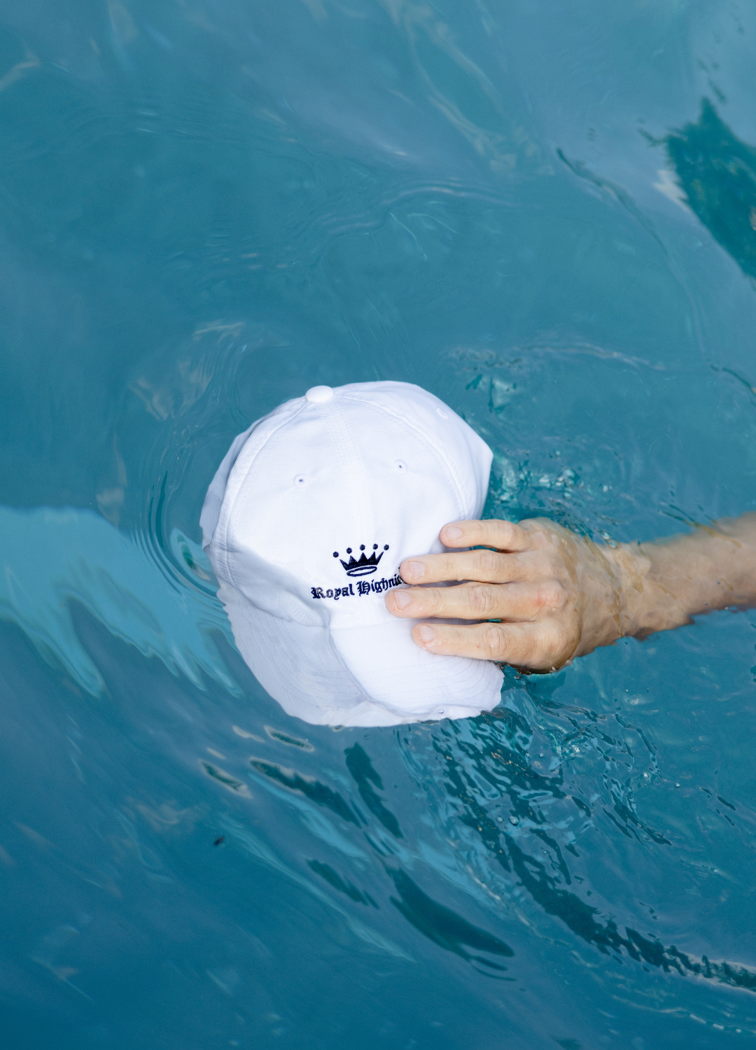 Hand holding a white cap above blue water