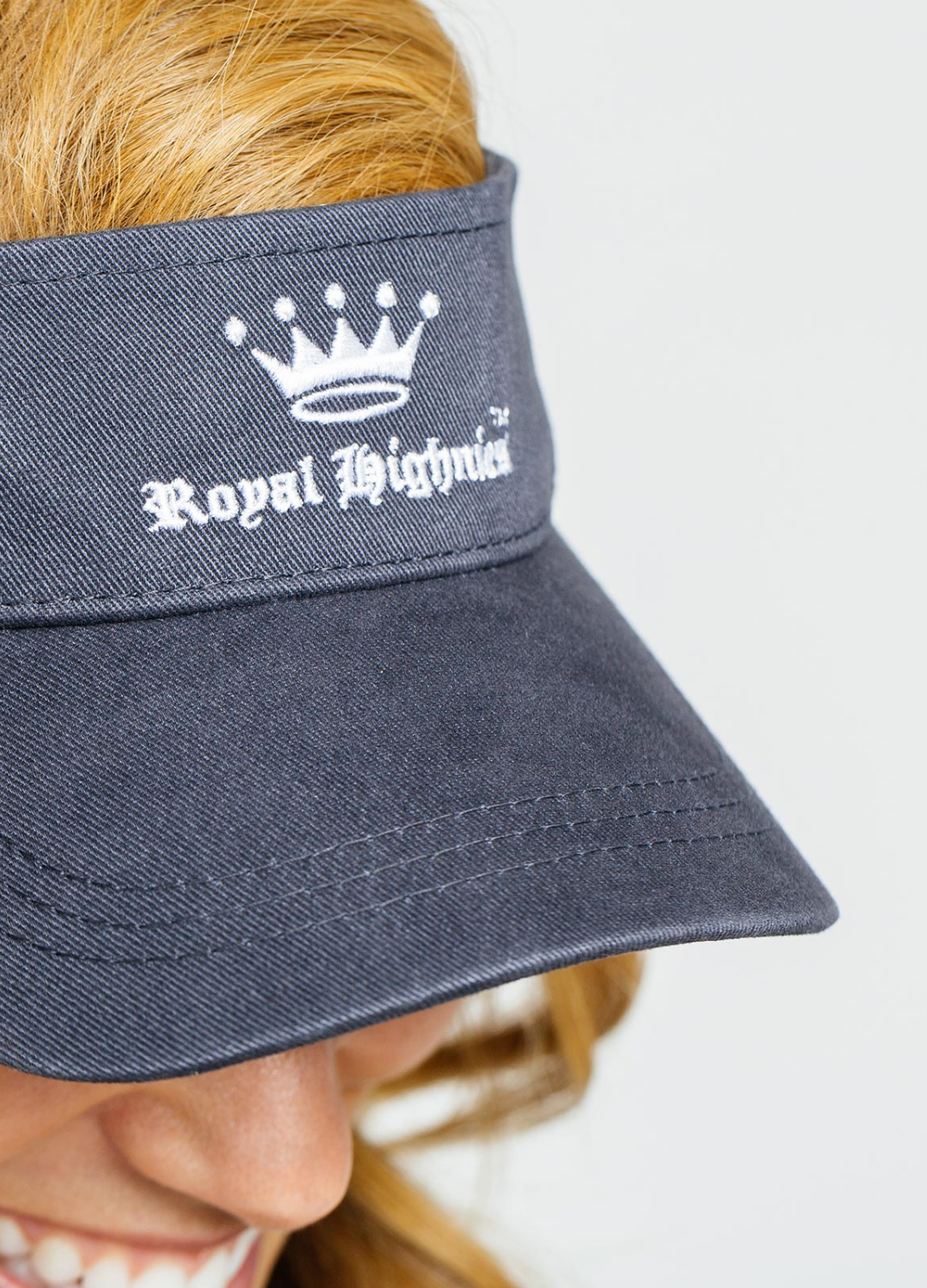 Navy blue visor with 'Royal Highness' logo worn by a person on a white background