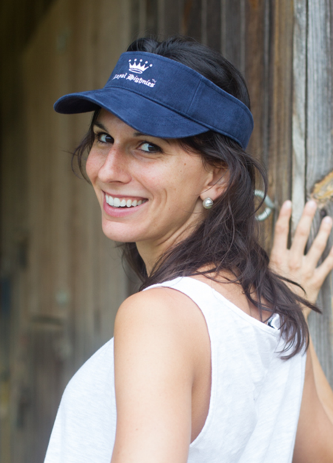 A woman wearing a navy blue visor with the 'Highnies' logo on it, smiling and standing in front of a wooden structure.