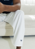 Man wearing white pants with navy logo sitting on a white couch