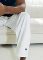 Man wearing white pants with navy logo sitting on a white couch