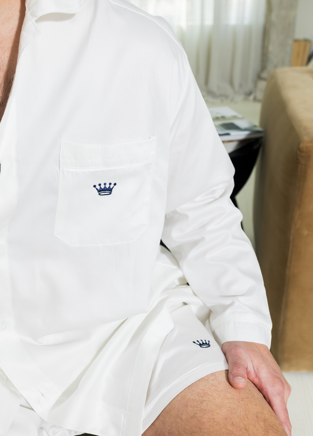 Person wearing a white long sleeve shirt with a small navy logo, sitting indoors.