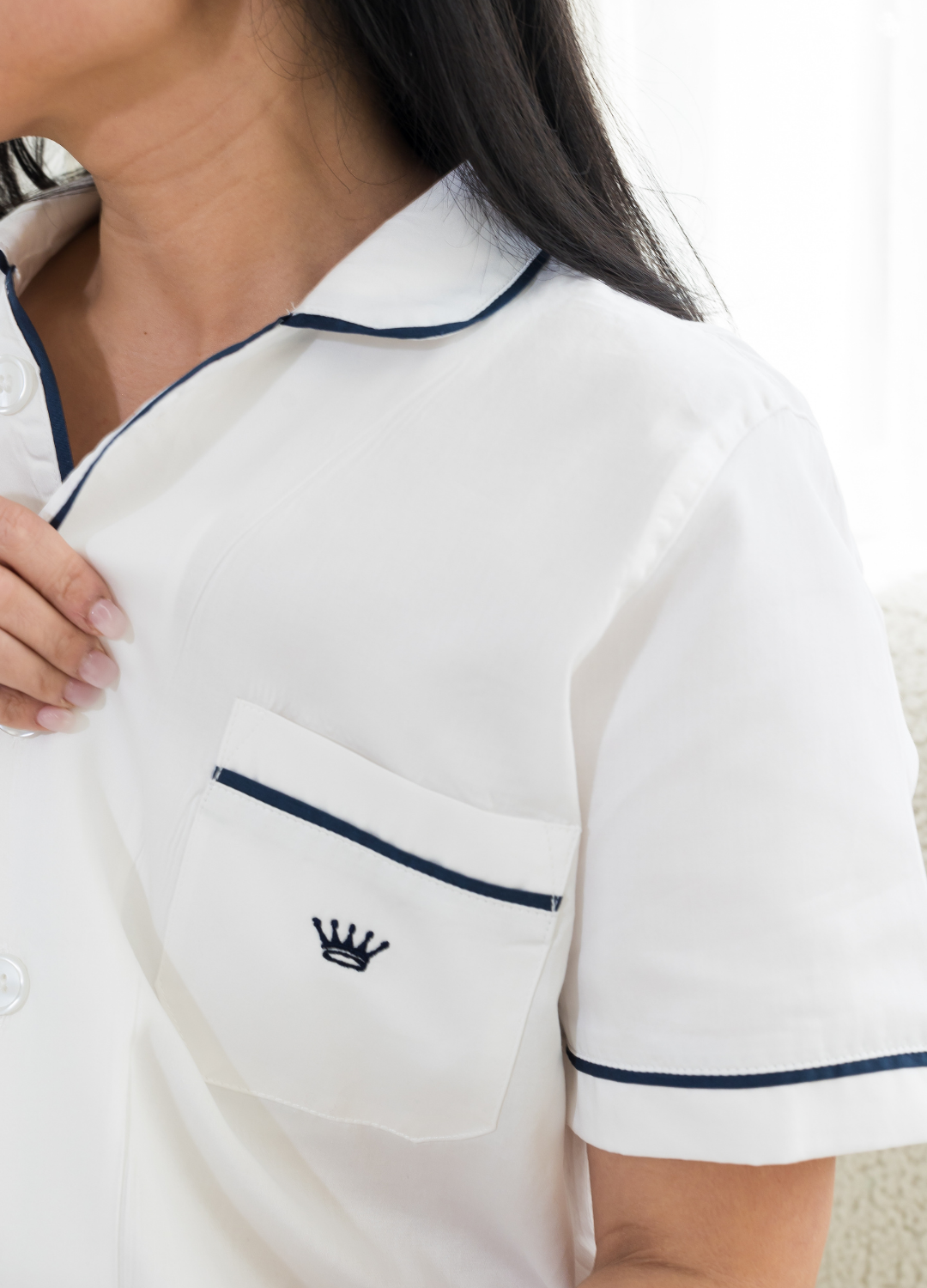 Woman wearing a white polo shirt with navy trim and crown logo, close-up on chest area.