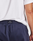 Close-up of a person wearing navy blue boxer shorts with an elastic waistband and a small black Royal Highnies label, paired with a white t-shirt.