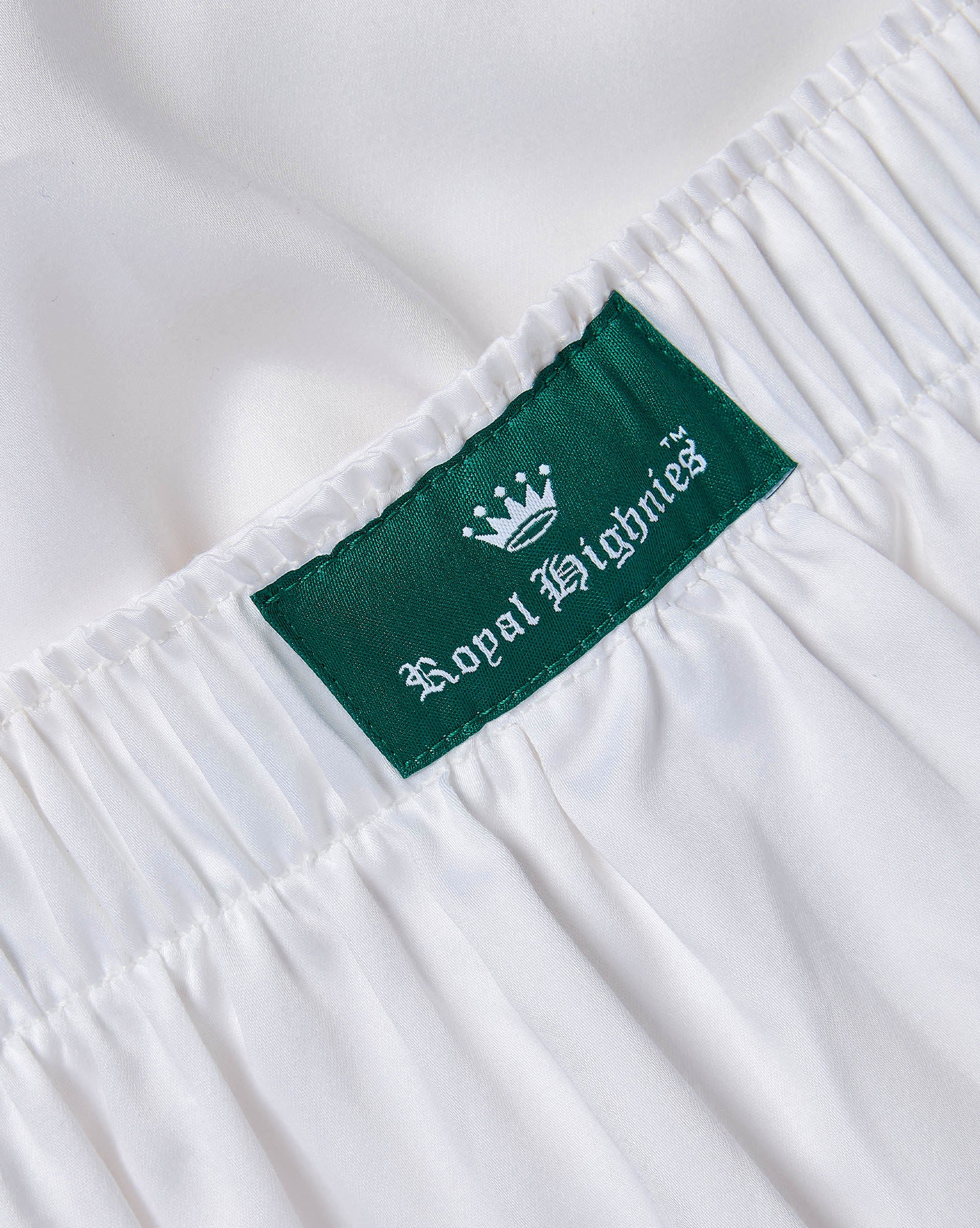 Close-up of a white garment with an elasticized waistband and a green fabric label reading 'Royal Highnies' with a white crown logo.