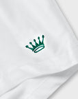 A close-up of a white fabric surface with a small embroidered crown logo in dark green.