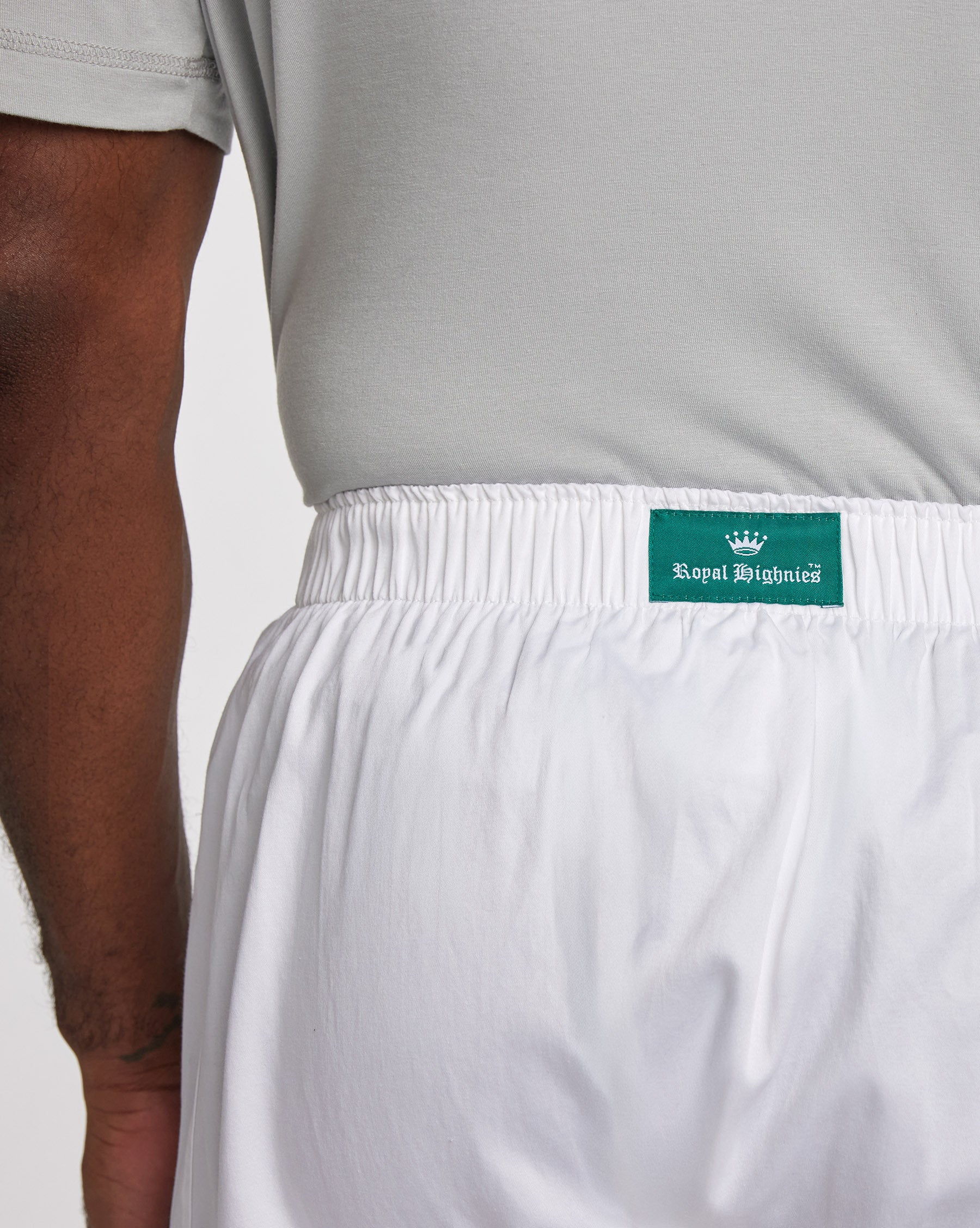 Close-up of a person wearing white boxer shorts with an elastic waistband and a green Royal Highnies brand patch, paired with a light gray t-shirt.