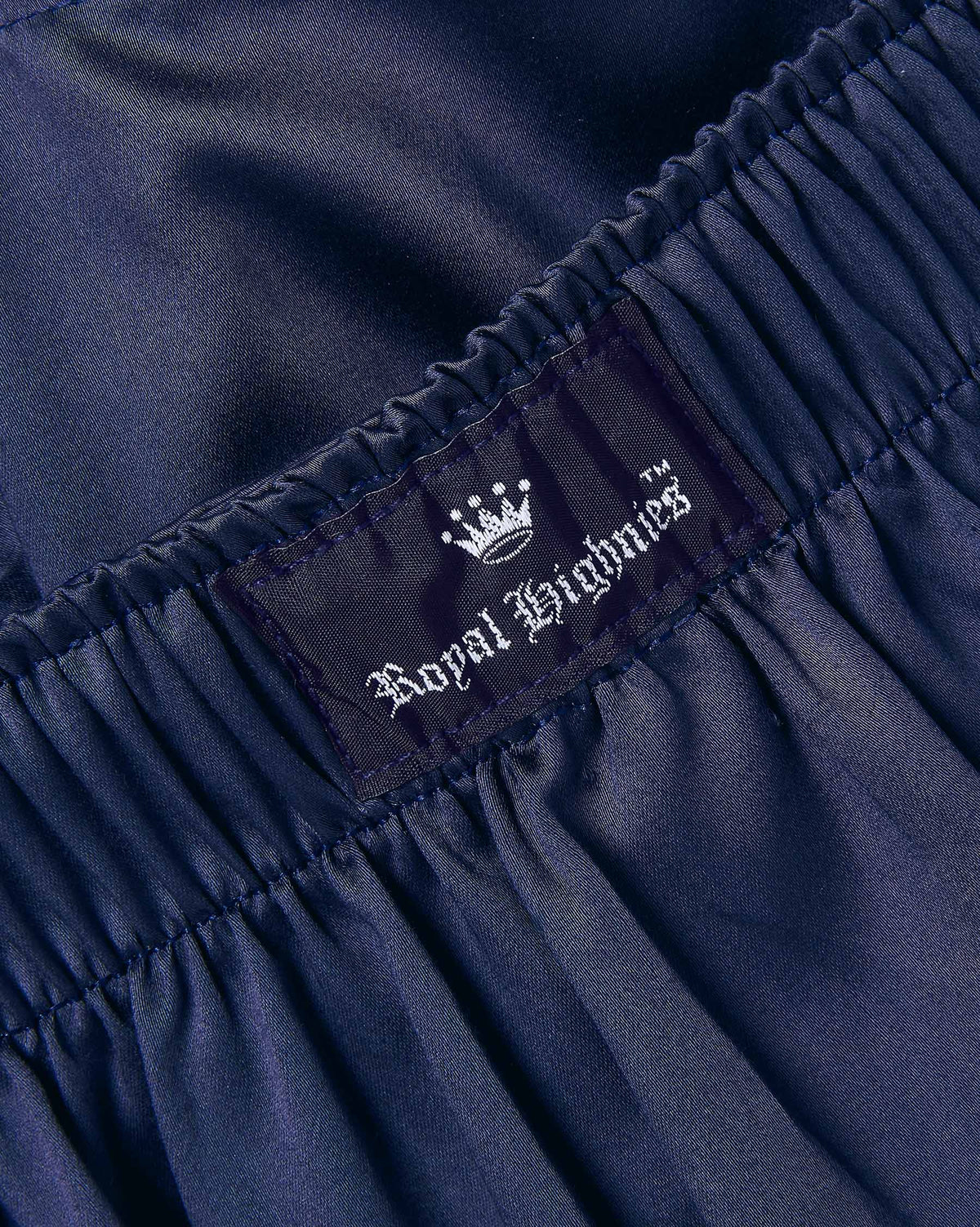 Close-up of dark navy blue gathered fabric with an elastic waistband and a sewn-in label reading Royal Highnies with a white crown logo.