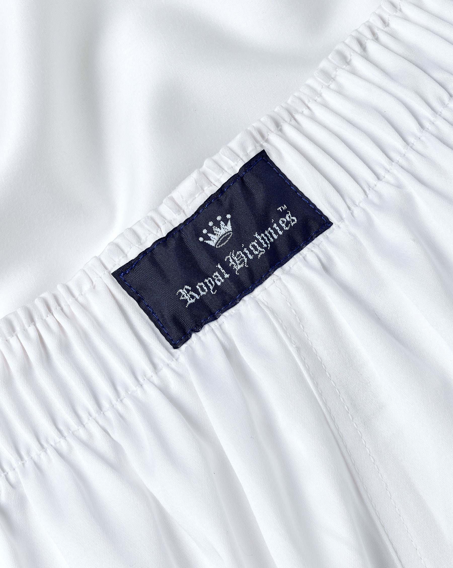Close-up of white elastic-waist fabric with a dark navy brand label reading Royal Highnies and a small crown logo.
