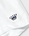 A close-up of a white fabric item, likely a shirt or garment, featuring a small navy embroidered crown logo on the chest.