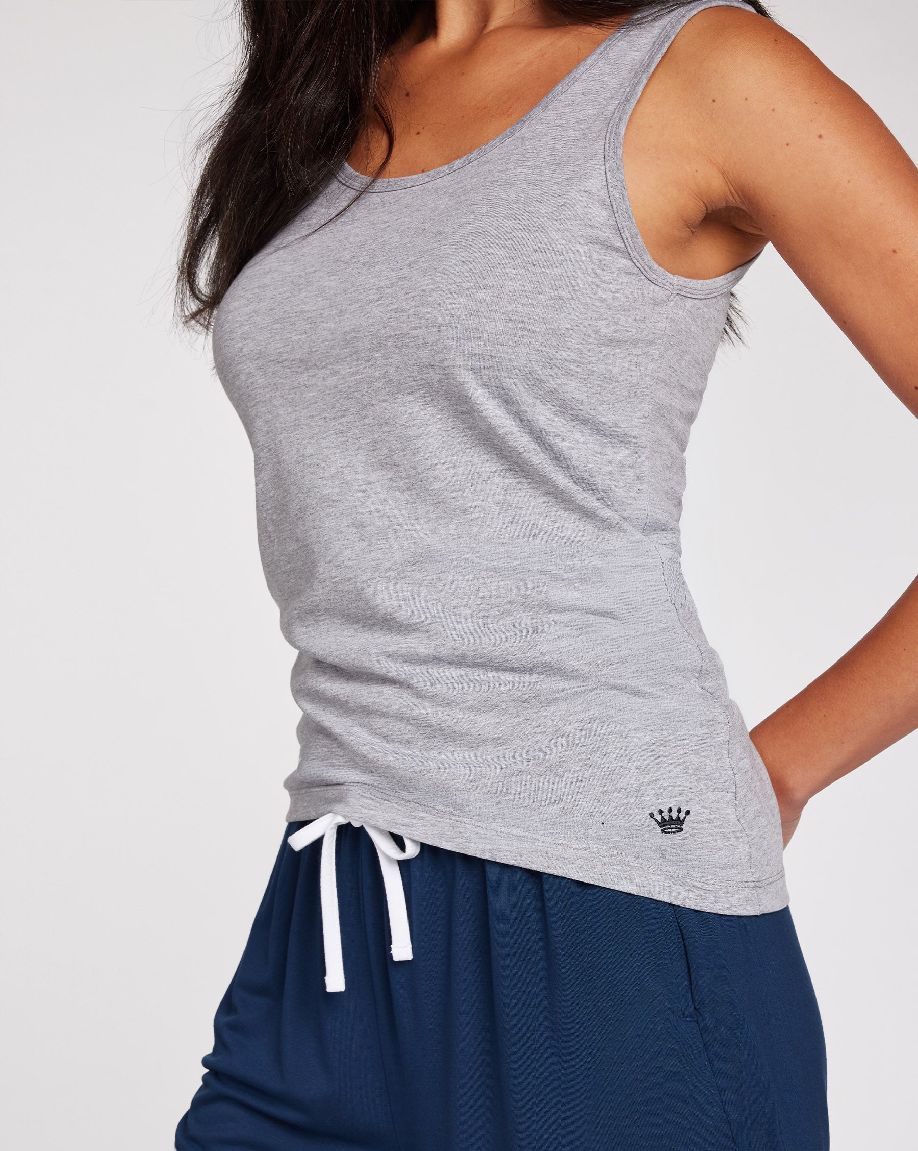 Woman wearing a light gray tank top and navy blue drawstring shorts, photographed against a clean light gray studio background.
