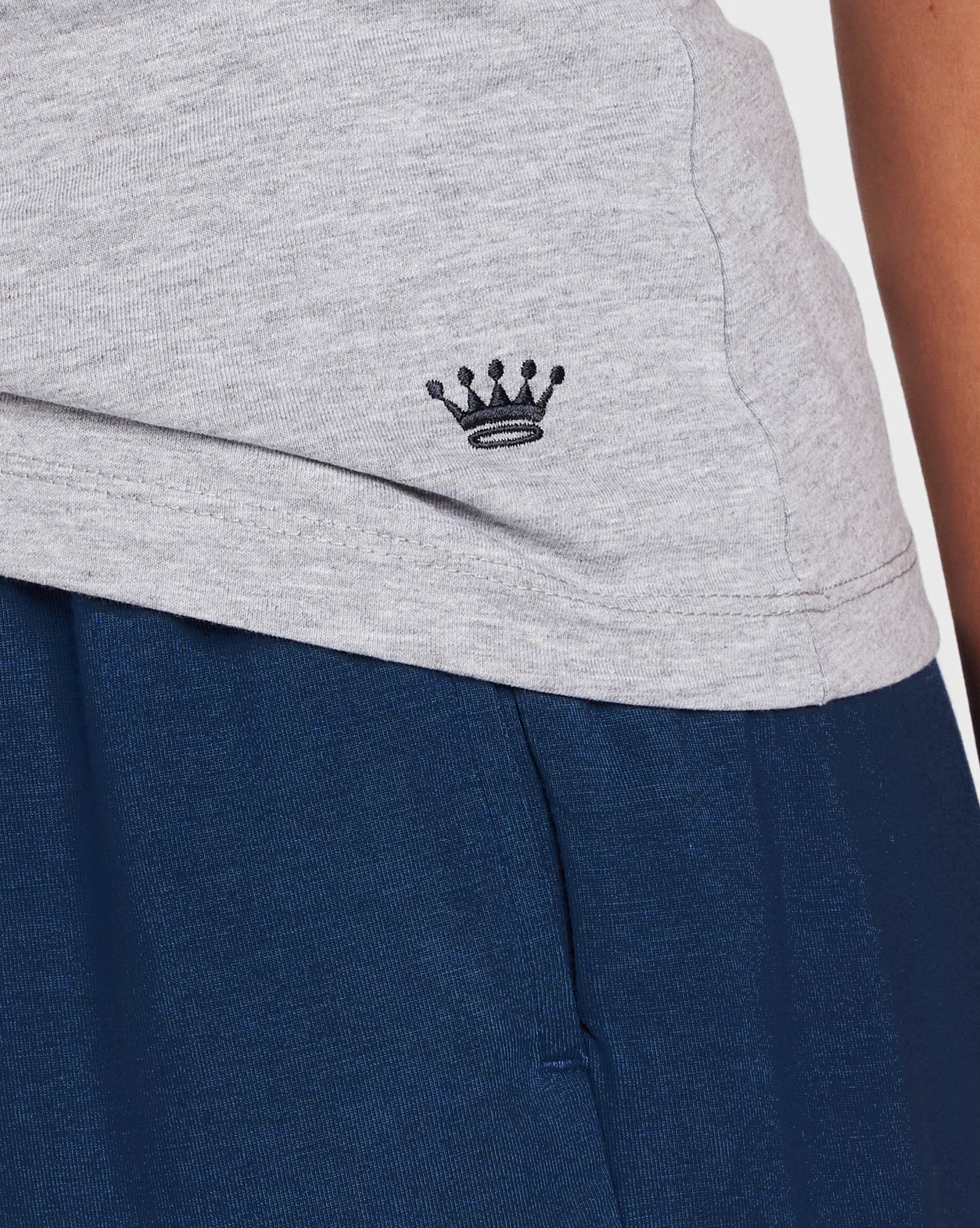Close-up of a light gray athletic top with a small navy embroidered crown logo, worn over dark navy shorts.