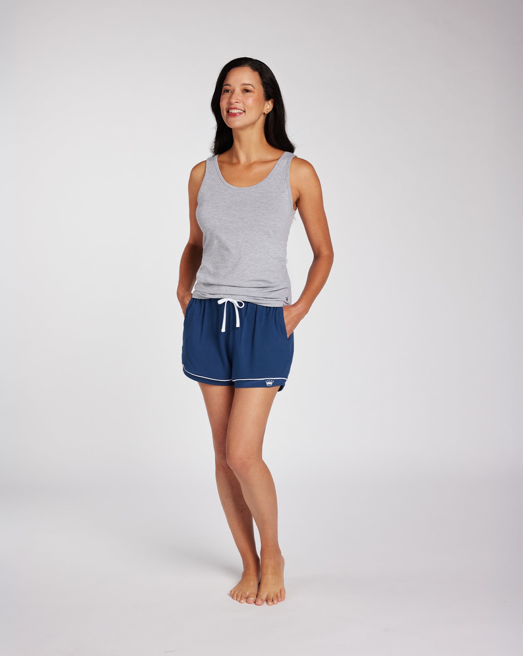 Woman wearing a light gray tank top and navy blue drawstring shorts, photographed against a clean light gray studio background.