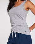 Woman wearing a light gray tank top and navy blue drawstring shorts, photographed against a clean light gray studio background.