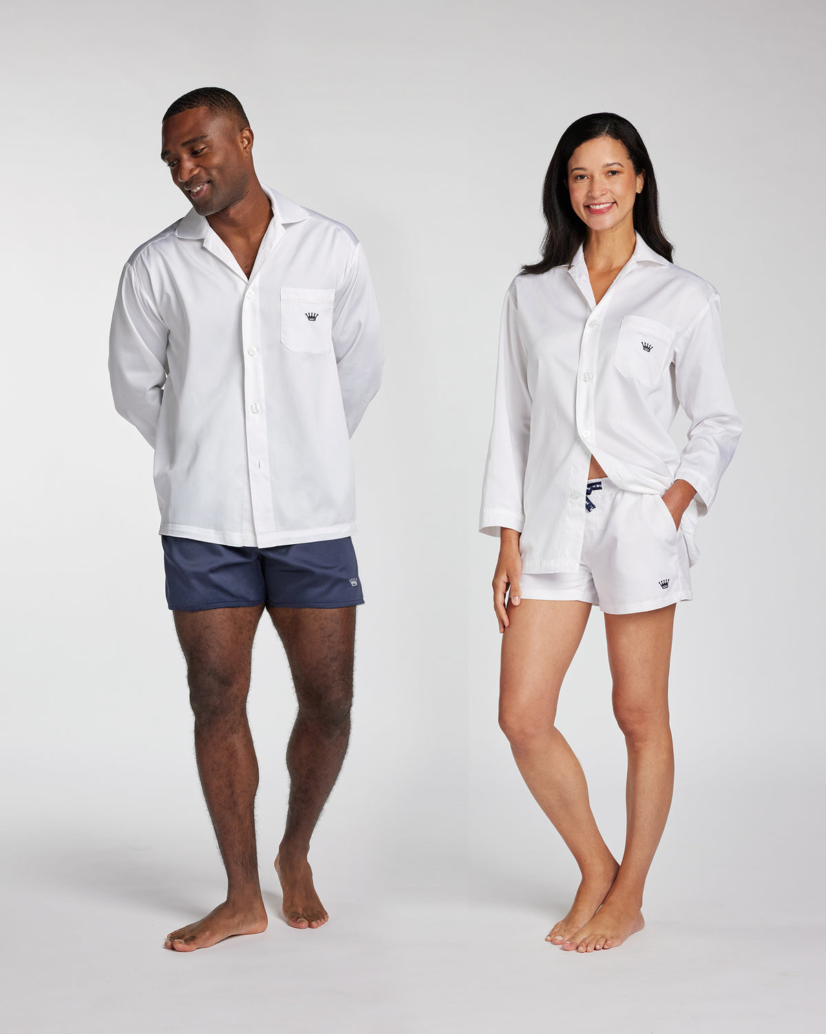 A man and a woman modeling matching white long-sleeve button-up pajama shirts and shorts sets against a light gray studio background.