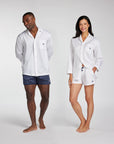 A man and a woman modeling matching white long-sleeve button-up pajama shirts and shorts sets against a light gray studio background.