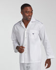 A man wearing a white long-sleeve button-front pajama top with a chest pocket and a small embroidered crown logo, photographed against a light gray studio background.