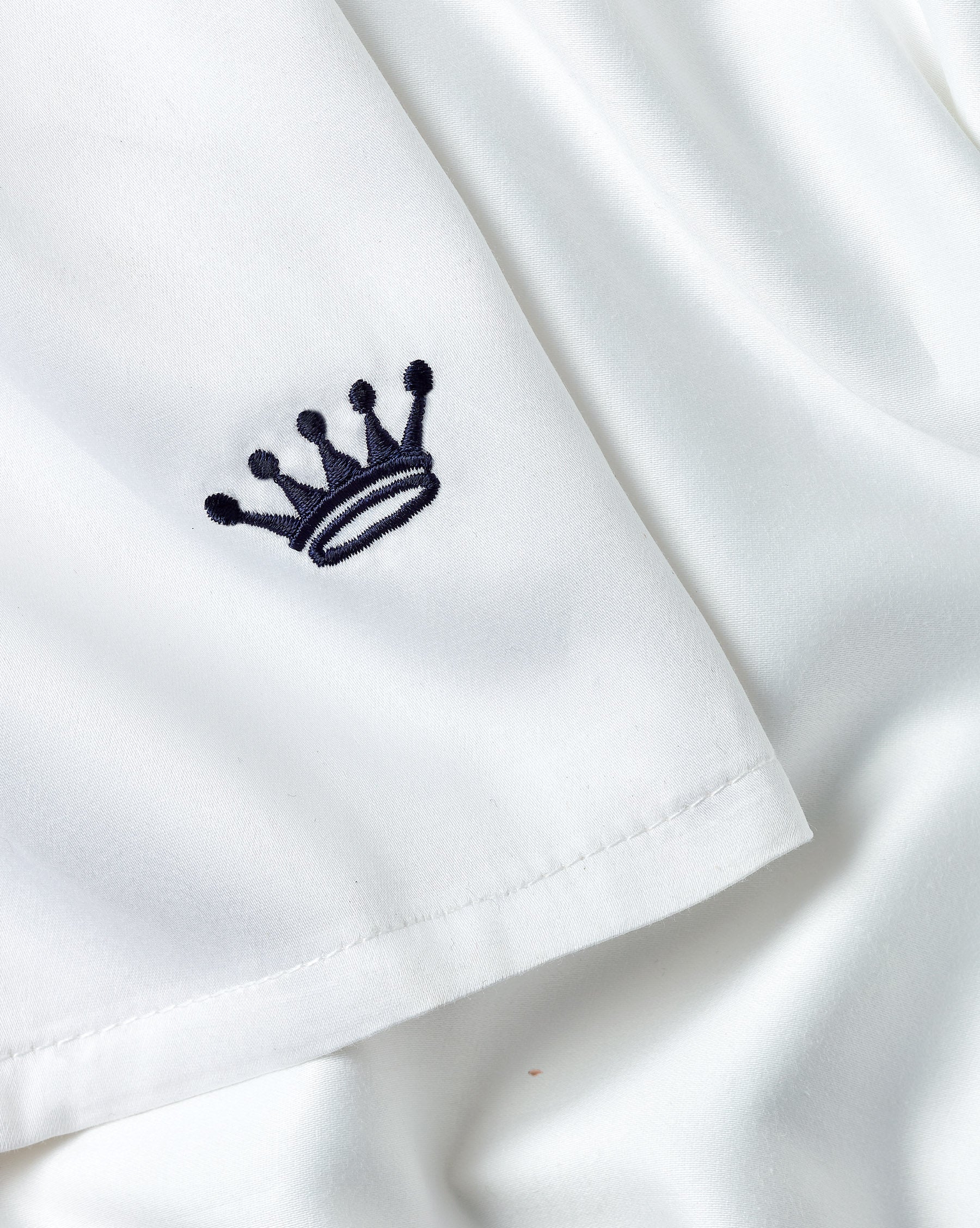 Close-up of a white fabric garment with a small navy embroidered crown logo on the sleeve.