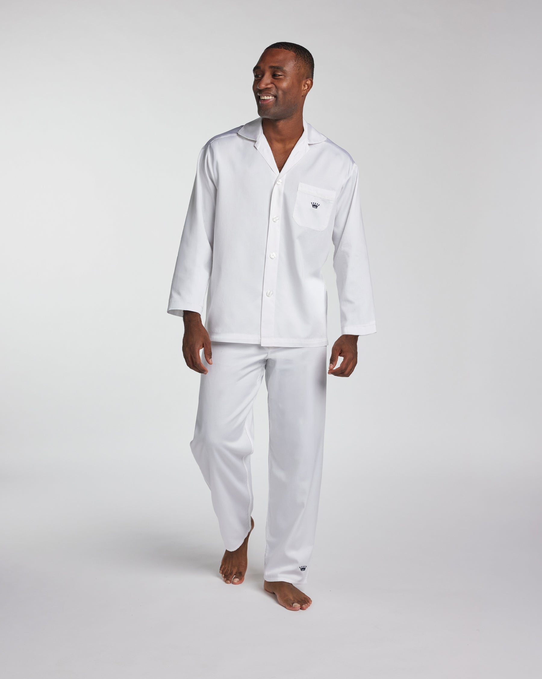 A man modeling a white long-sleeve pajama set with a button-front shirt and matching pants against a light gray studio background.