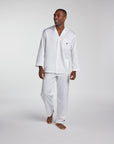 A man modeling a white long-sleeve pajama set with a button-front shirt and matching pants against a light gray studio background.