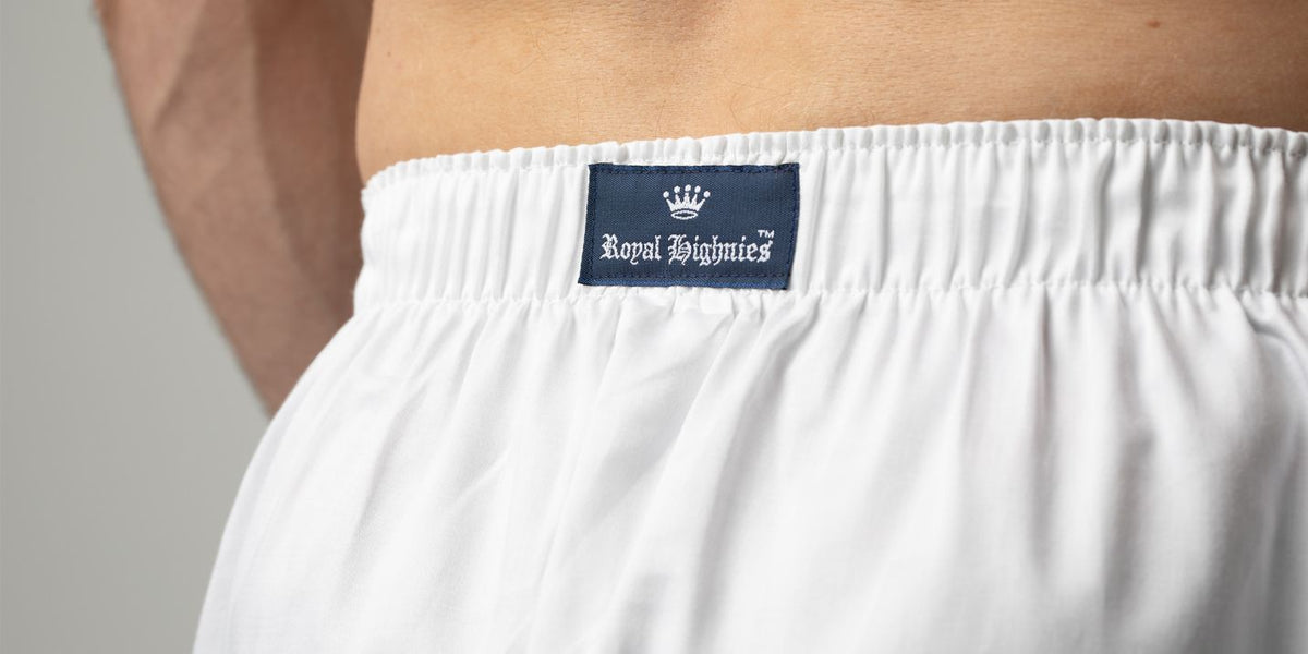 Close-up of a person wearing white boxer briefs, showing the elastic waistband with a navy blue Royal Highnies brand label.