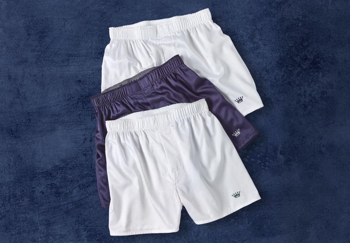 Three pairs of shorts, two white and one purple, on a textured blue background.